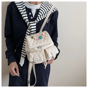 Detail of a creamy white quilted backpack with colorful bead handle and front pockets