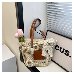 Close-up of woven straw tote bag featuring brown leather straps and a white lace bow detail