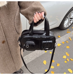 Close-up of a glossy black crossbody bag featuring dual pockets and silver hardware