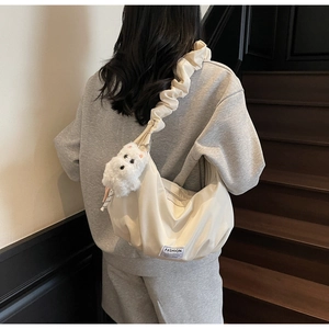 Detail view of cream dumpling bag with ruffled strap and plush bear charm on a model