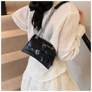 Detail of a black patent leather crossbody bag featuring silver chains and buckles
