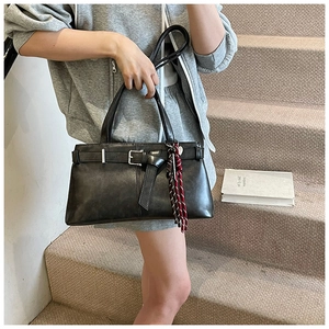 Detail of matte faux leather shoulder bag with silver buckle and woven tassel charm