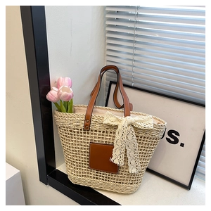 Detail of woven straw tote bag with brown leather handles and decorative white lace bow