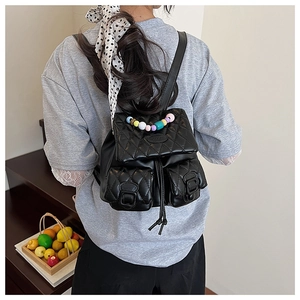 Rear view of model wearing a black quilted backpack with colorful beaded handle detail