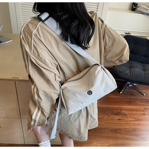 Close-up of a light grey nylon crossbody bag with metallic logo on a casual trench coat