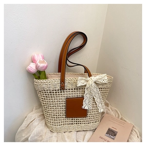 Detail of woven straw tote bag featuring brown leather patch and white lace bow