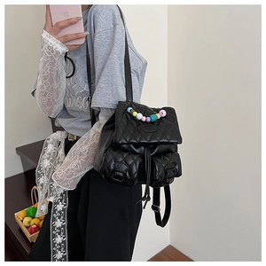Black quilted backpack with macaron-colored bead handle on a model in a casual setting