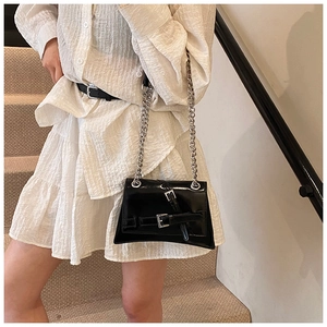 Detail of a black glossy crossbody bag featuring dual metal buckles and silver chain strap