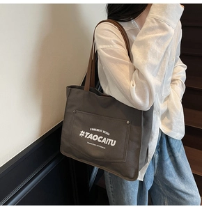 Detail of grey canvas tote bag with brown straps and front pocket shown on model