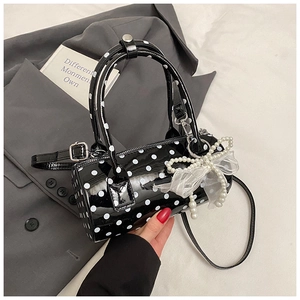 Détail d'un sac cylindrique noir à pois avec un pendentif nœud en maille et perles