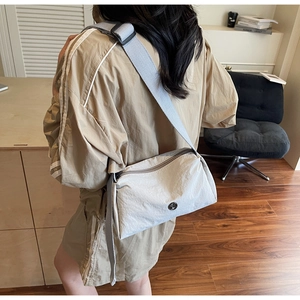 Detail of beige nylon crossbody bag featuring an adjustable wide strap on a model