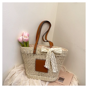 Detail of straw tote bag with brown leather handles and decorative white lace bow