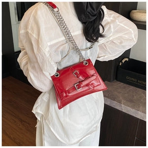 Detail of red asymmetrical crossbody bag with silver chain strap and metal buckles