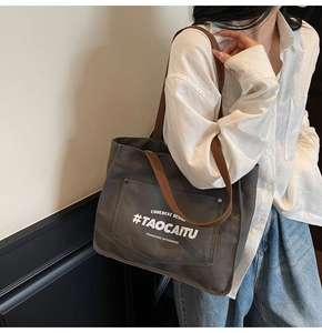 Detail of dark grey canvas tote bag with brown straps worn on the shoulder by a model