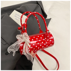 Détail du sac cylindre rouge à pois avec breloque en perle et nœud en organza blanc