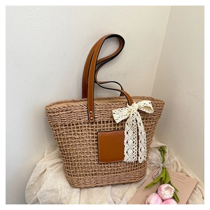 Detail of hand-woven straw tote bag with brown leather handles and white lace bow accessory