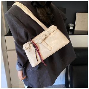 Detail of beige shoulder bag featuring metal buckle strap, silk scarf, and key charm
