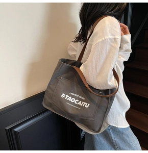 Detail of grey canvas tote bag with brown straps worn by a model in a modern room