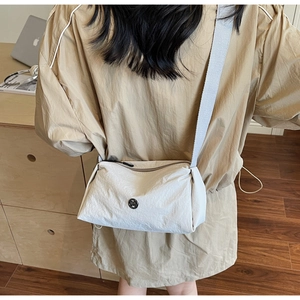 Close-up of minimalist cream crossbody bag with a round black metal logo and woven strap