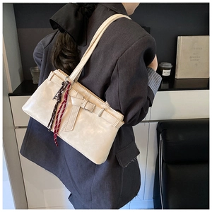 Detail of a beige leather shoulder bag featuring a belt buckle and woven rope charms
