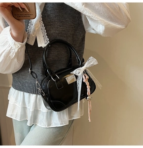 Nahaufnahme der schwarzen Lackleder-Boston-Tasche mit Spitzenschleife und Anhängern