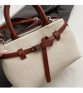 Close-up of canvas bucket bag with brown leather trim and metallic buckle details