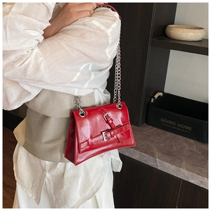 Detail of red patent leather crossbody bag with silver double chain and buckle strap