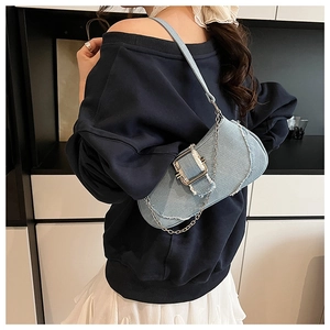 Detail of light blue denim shoulder bag with silver buckle and chain on model