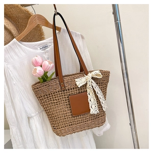 Detail of woven straw beach tote with leather handles and a white lace bow decoration