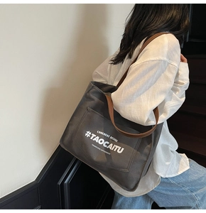 Close-up of charcoal canvas tote bag with brown leather handles and printed text