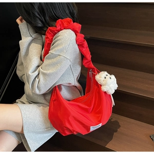 Detail of red crescent bag with pleated straps, fashion label and plush dog charm