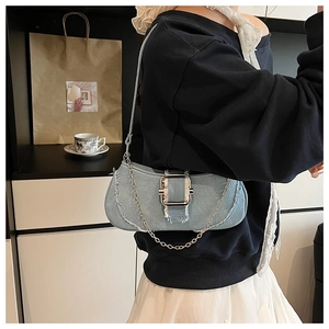 Detail of frayed denim shoulder bag featuring a bold silver buckle and metal chain strap