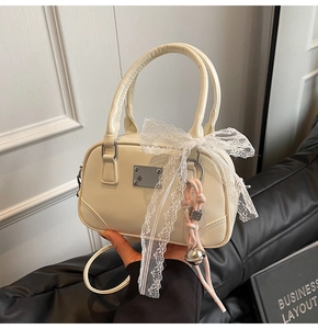 Detailansicht der cremefarbenen Lackledertasche mit Spitzenschleife und Anhänger