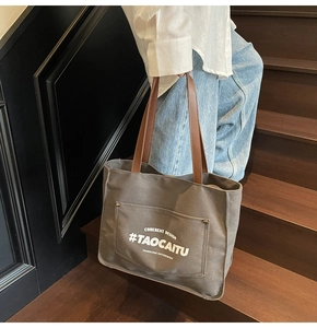 Detail view of large grey canvas tote bag with brown leather straps and printed graphics