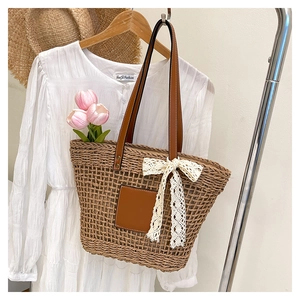 Close-up of woven straw tote bag featuring leather handles and a delicate lace bow