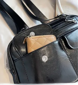 Detail of black leather tote with silver zippers and a beige quilted wallet inside