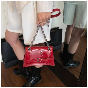 Detail of red glossy leather shoulder bag with silver buckle and chunky chain strap