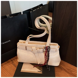 Detail view of cream leather shoulder bag featuring decorative buckle and woven charm