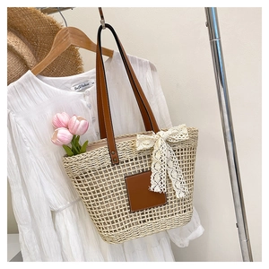 Detail of beige straw tote bag with brown leather handles and white lace bow decoration