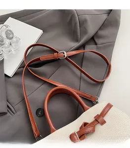 Detail of cream canvas and brown leather bucket bag placed on a grey blazer