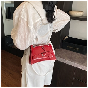 Detailed view of red glossy crossbody bag featuring silver chain strap and belt buckle decor