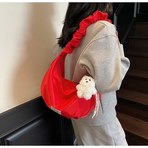 Detail of red crescent bag with ruffled strap and plush bear charm on a female model