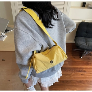 Detail of bright yellow crossbody bag with metal M logo and adjustable nylon strap