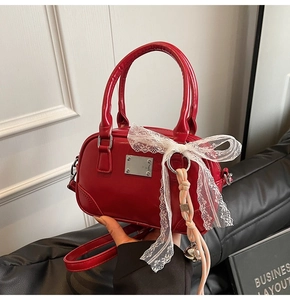 Detail der roten glänzenden Ledertasche mit weißer Spitzenschleife und Silberbeschlägen