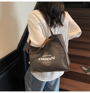 Detail of dark grey canvas tote bag with brown straps worn on a model's shoulder