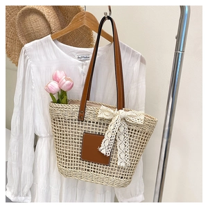Detail of hand-woven straw tote bag featuring leather straps and a lace bow decoration