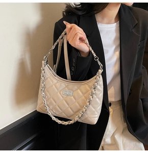 Detail der beigen gesteppten Schultertasche mit Silberkette und Drehverschluss am Model