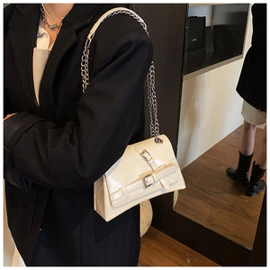 Close-up of cream white glossy leather shoulder bag with silver chain and buckles