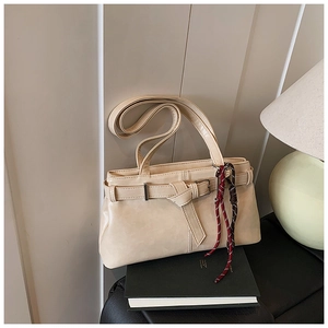 Close-up of a cream retro shoulder bag with belt buckle and woven pendant detail