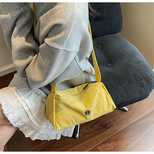 Detail of bright yellow crossbody pillow bag with wide strap and metallic M logo